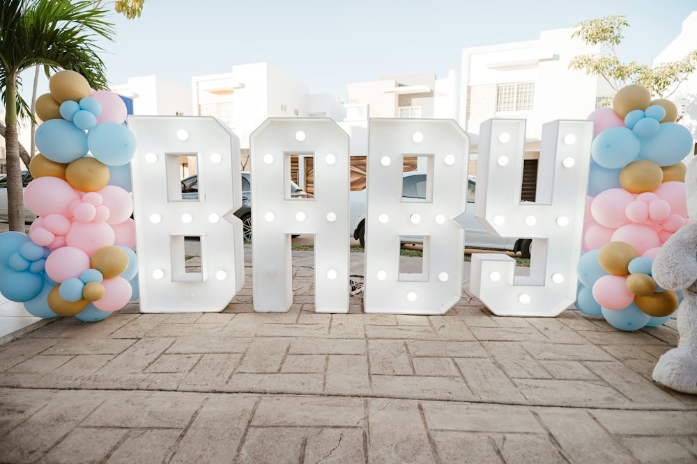 Grote verlichte letters BABY tussen roze en blauwe ballonnen